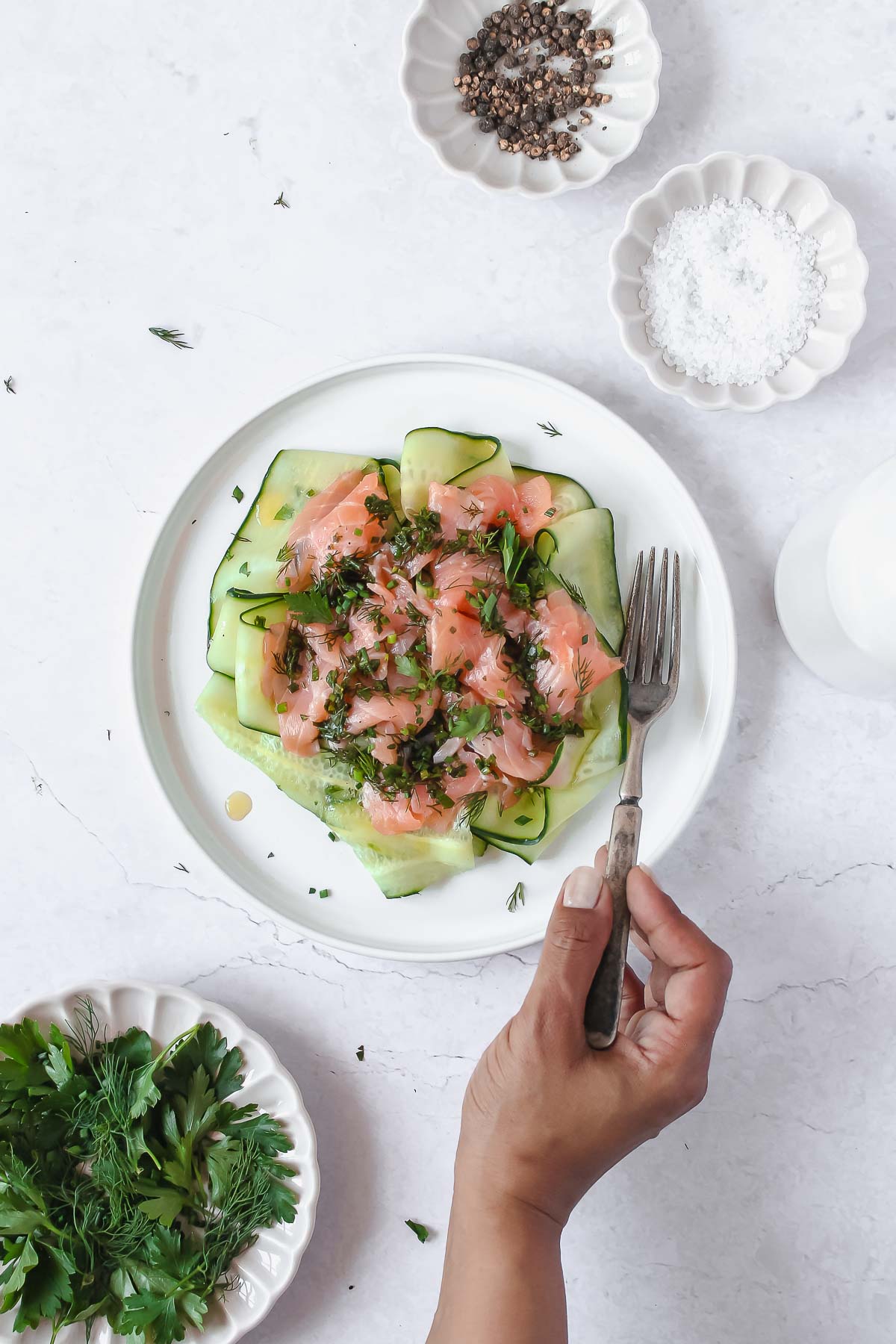 smoked salmon with herb vinaigrette and cucumber on white plate with vintage fork.