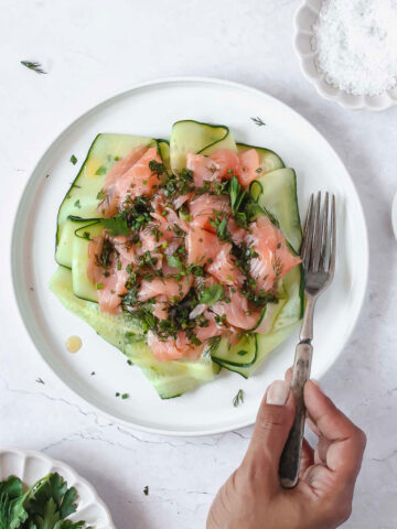 smoked salmon with herb vinaigrette and cucumber on white plate with vintage fork.