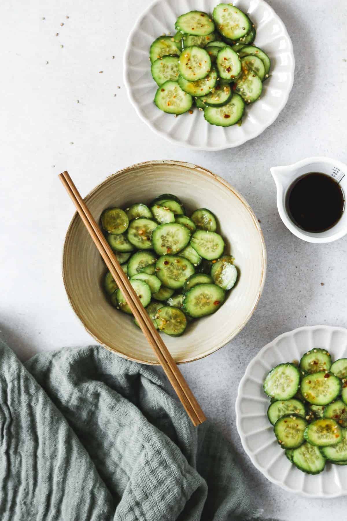 spicy asian cucumber salad on beige plates with chopsticks and dressing on light background.