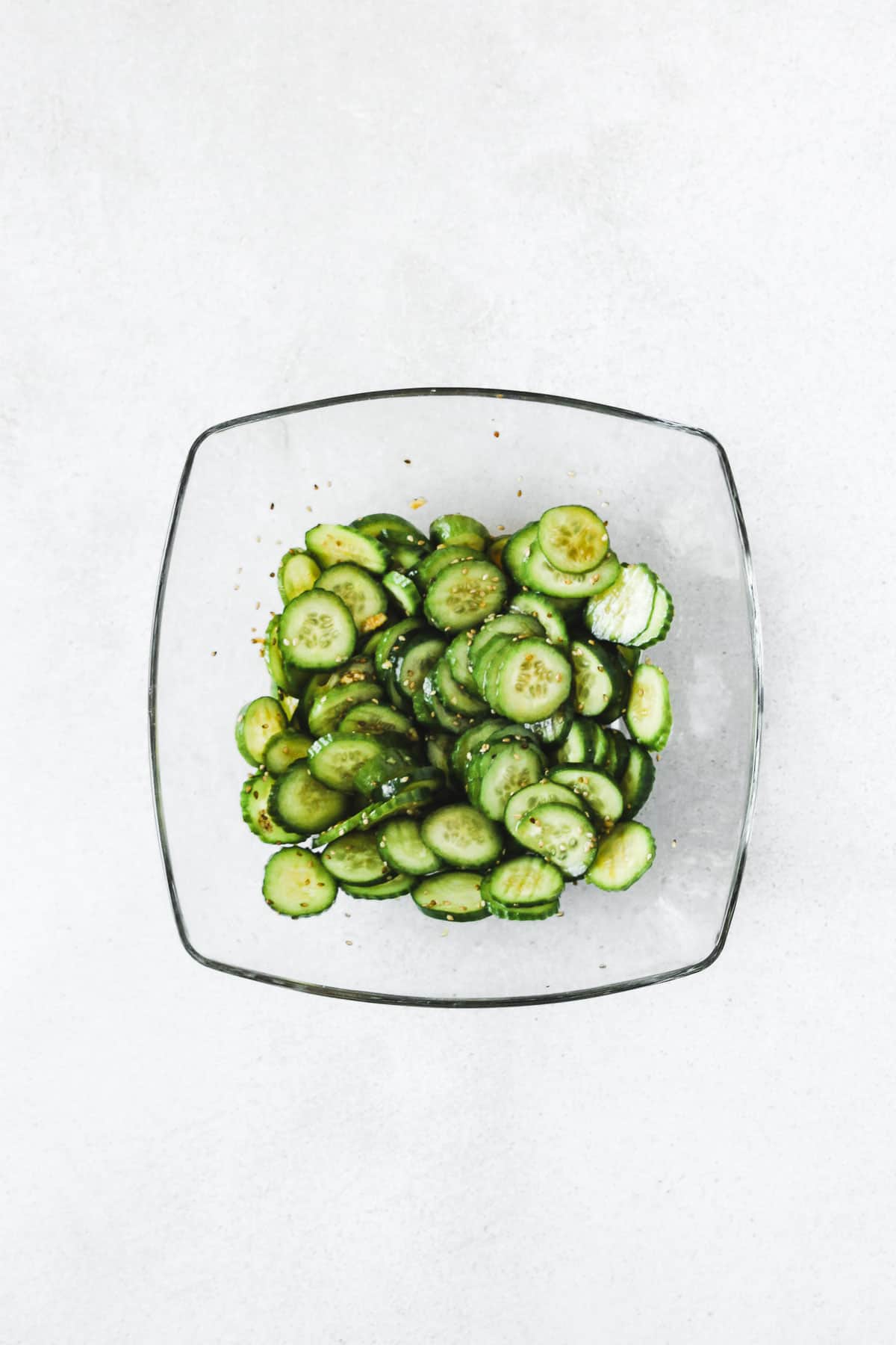 sliced cucumber mixed with asian-inspired dressing in glass bowl on light background.