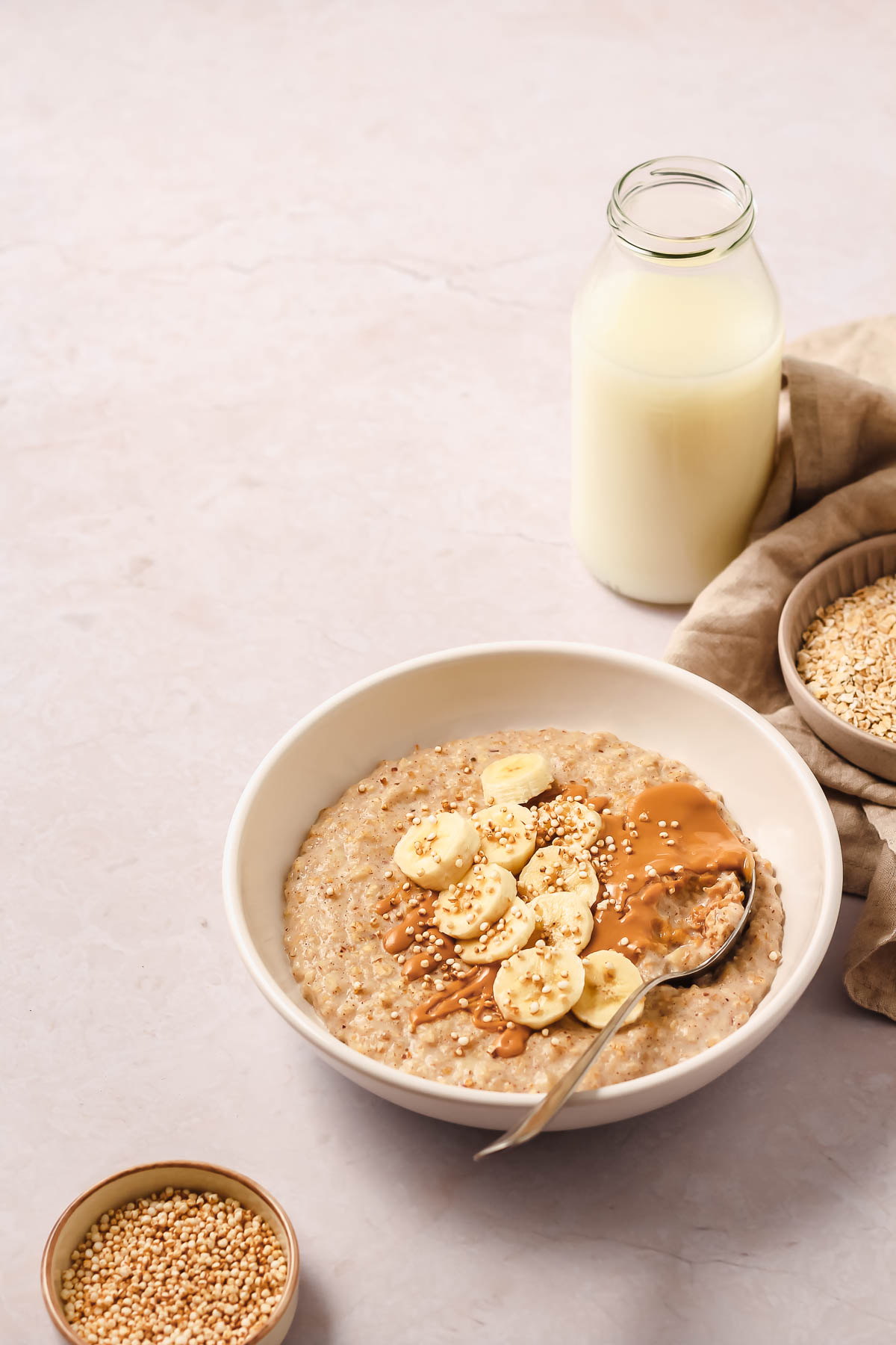 banana porridge with toppings on white bowl with vintage spoon and props on rosy background.