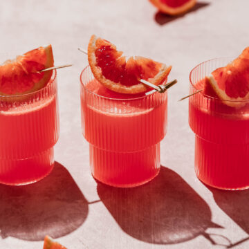 blood orange vodka cocktail with blood orange slice garnish on rosy background.