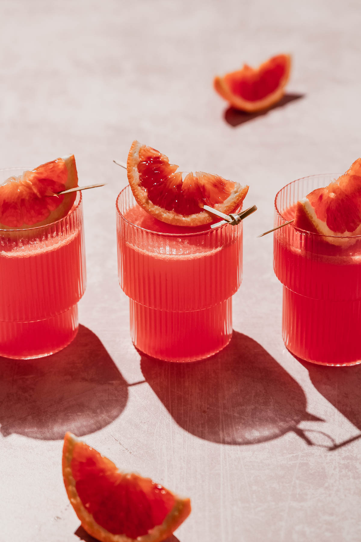 blood orange vodka cocktail with blood orange slice garnish on rosy background.