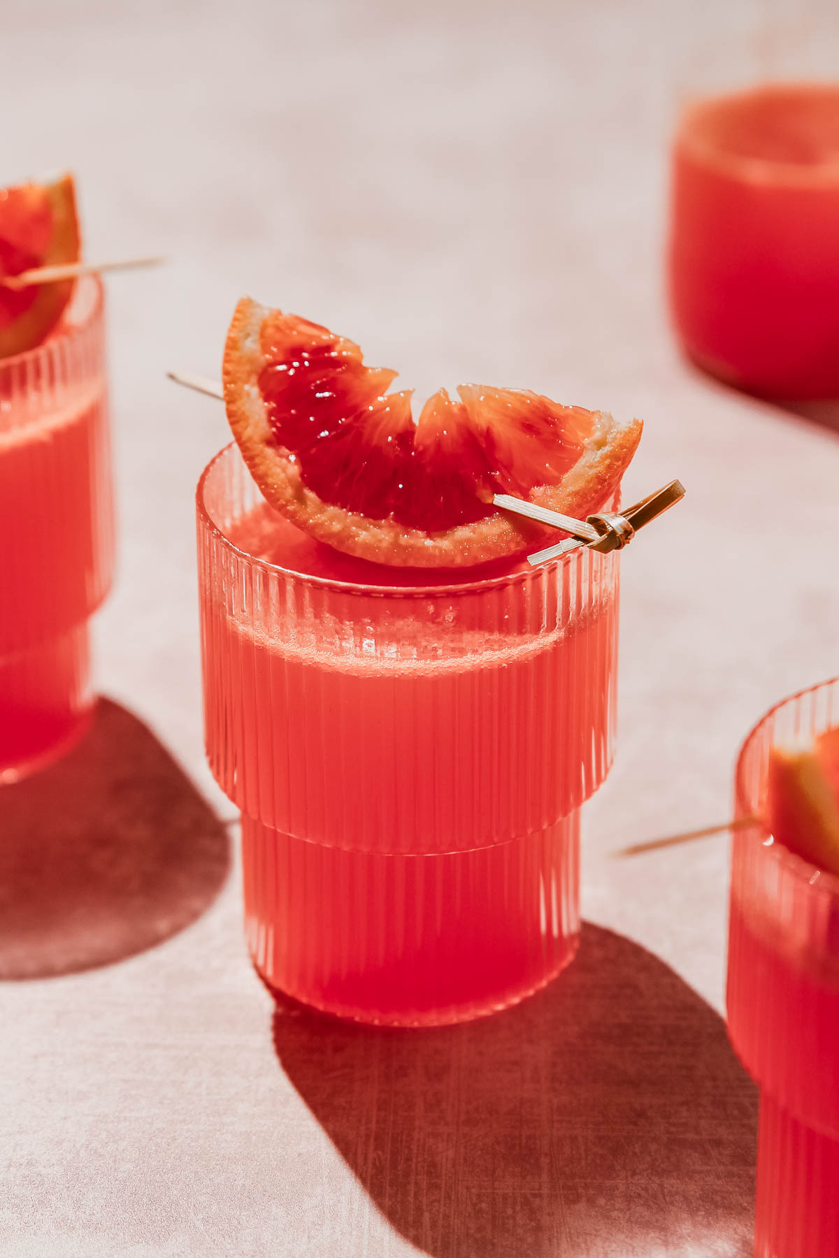 citrus vodka cocktail with blood orange garnish ob rosy background.