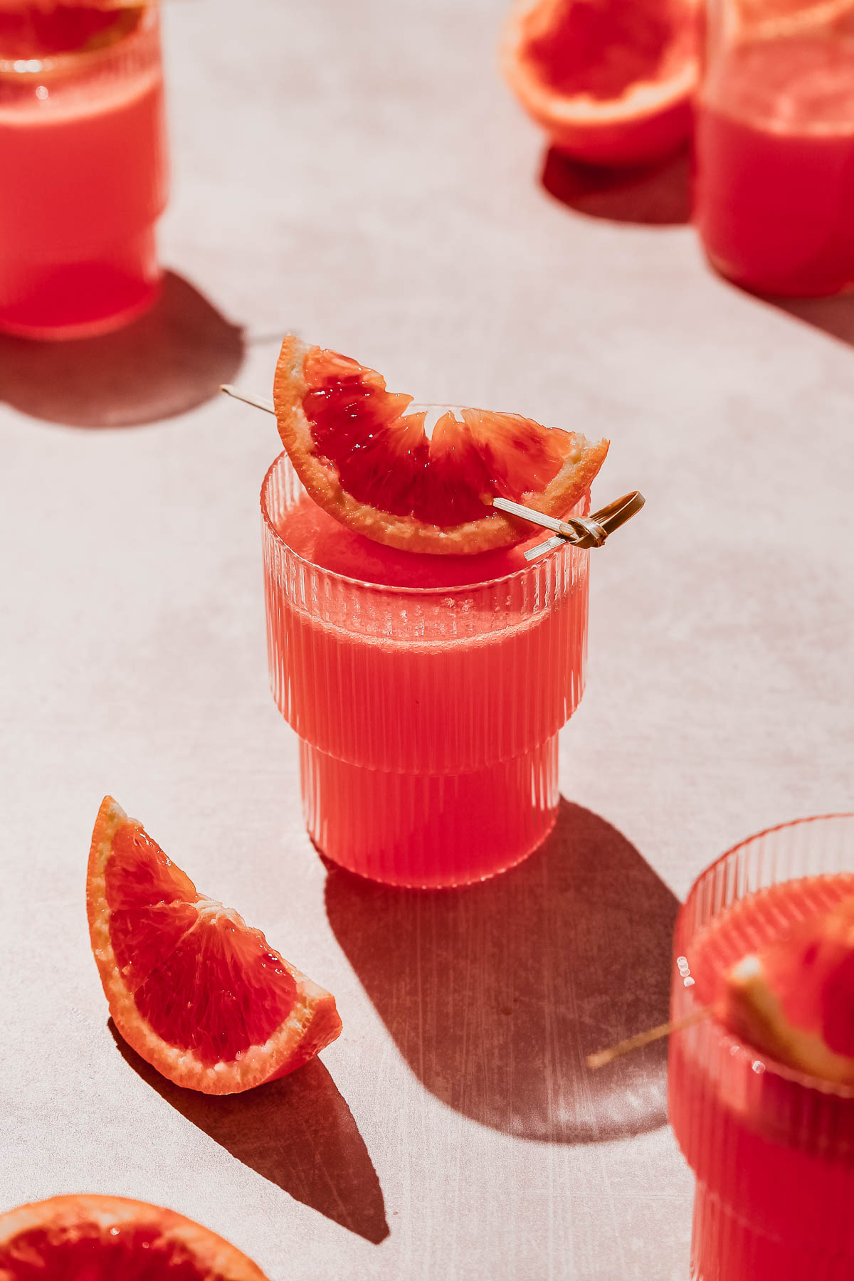 citrus vodka cocktail with blood orange garnish ob rosy background.