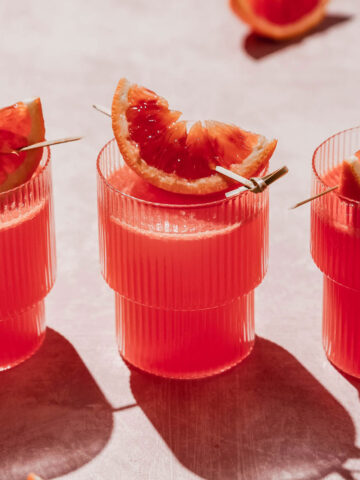 blood orange vodka cocktail with blood orange slice garnish on rosy background.