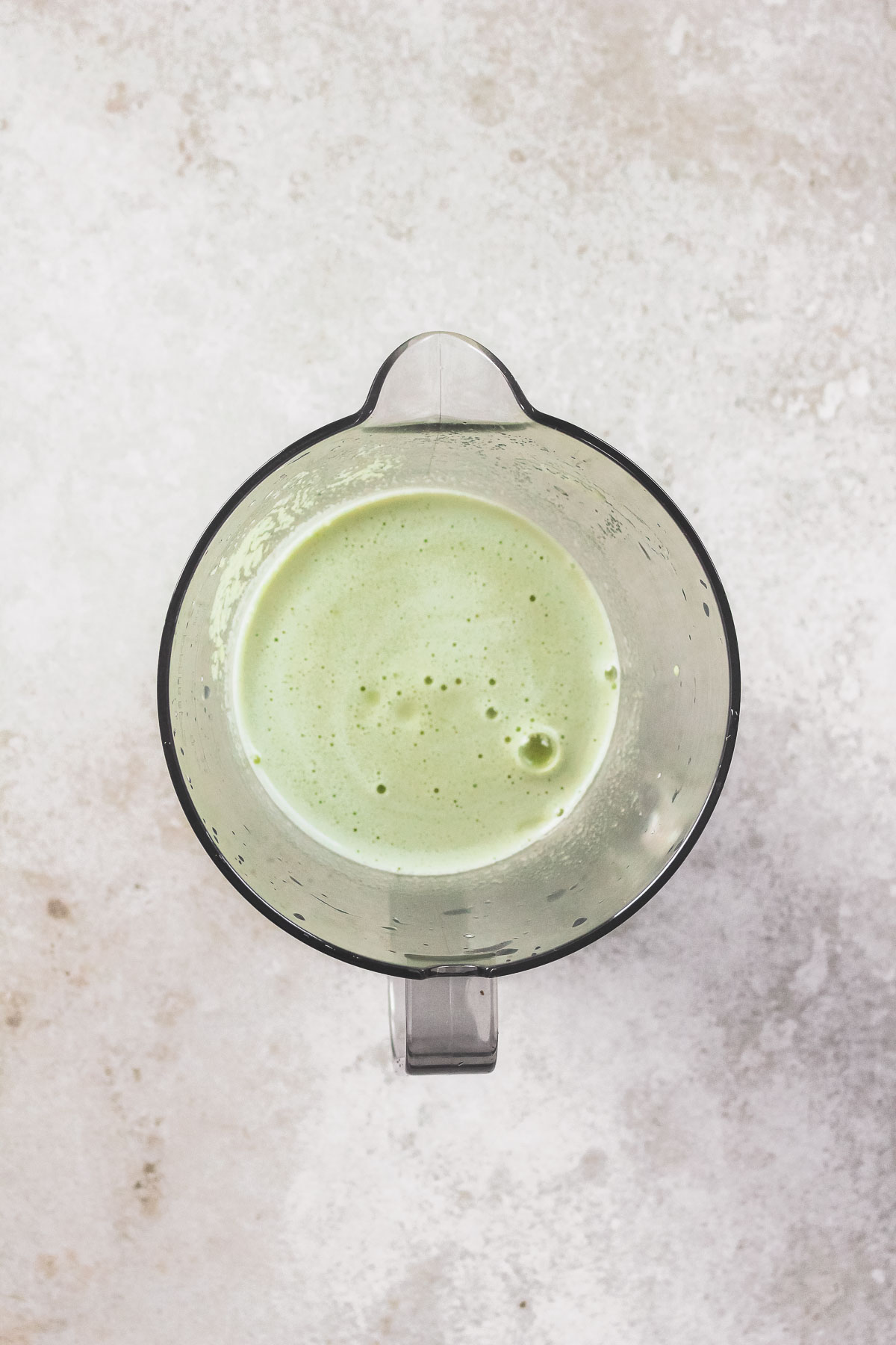 freshly pressed green juice in pitcher on beige background.