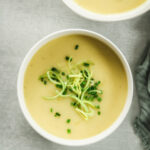 low carb potato and leek soup in white bowls on green background with linen and drinking glass.