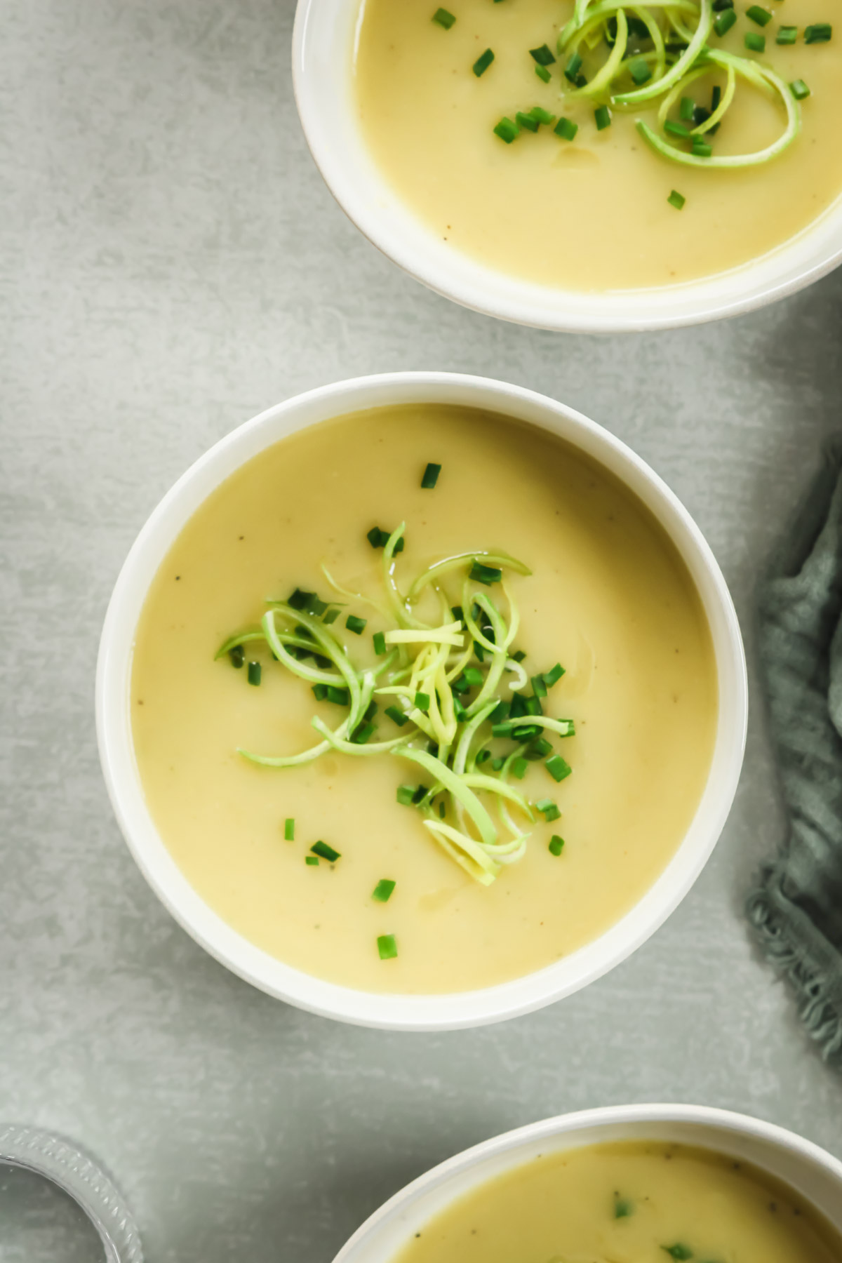 low carb potato leek soup in white bowls on green background with linen and drinking glass.