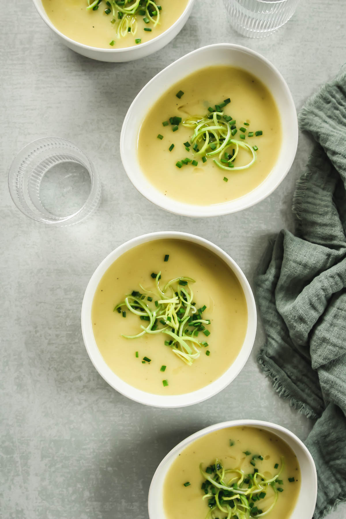 healthy potato and leek soup without cream in white bowls on green background with linen and drinking glass.