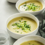 healthy potato and leek soup without cream in white bowls on green background with linen and drinking glass.
