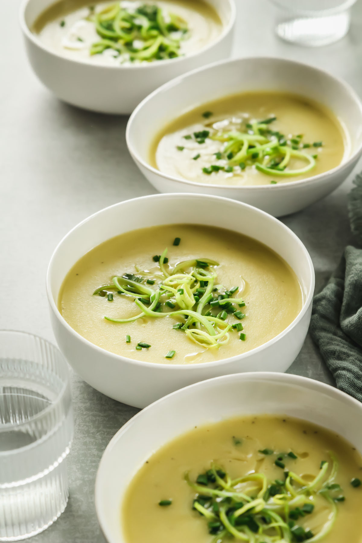 healthy potato and leek soup without cream in white bowls on green background with linen and drinking glass.