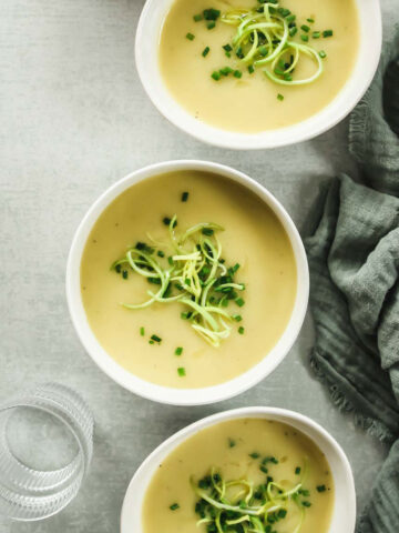 vegan potato leek soup in white bowls on green background with linen and drinking glass.