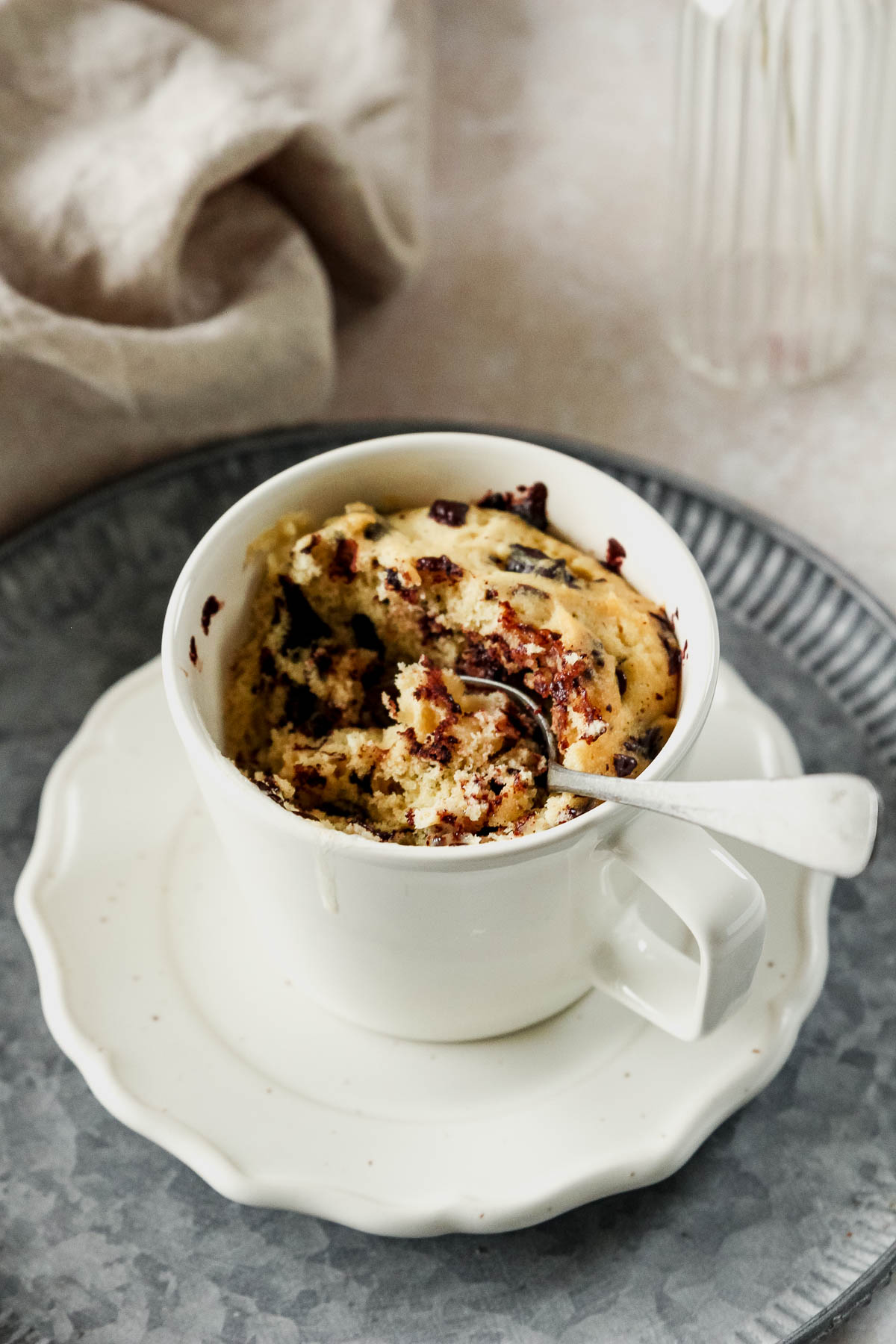 chocolate chip mug cake in off-white mug with vintage spoon in cake.