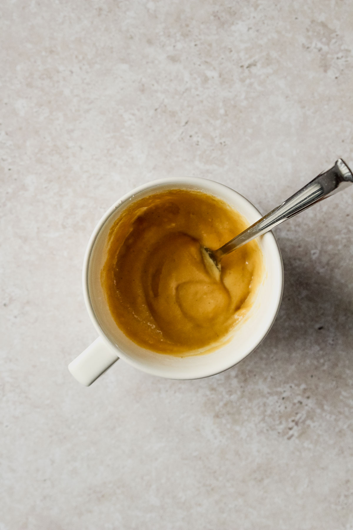 mixed dough for chocolate almond flour mug cake in off-white mug on beige marble background.