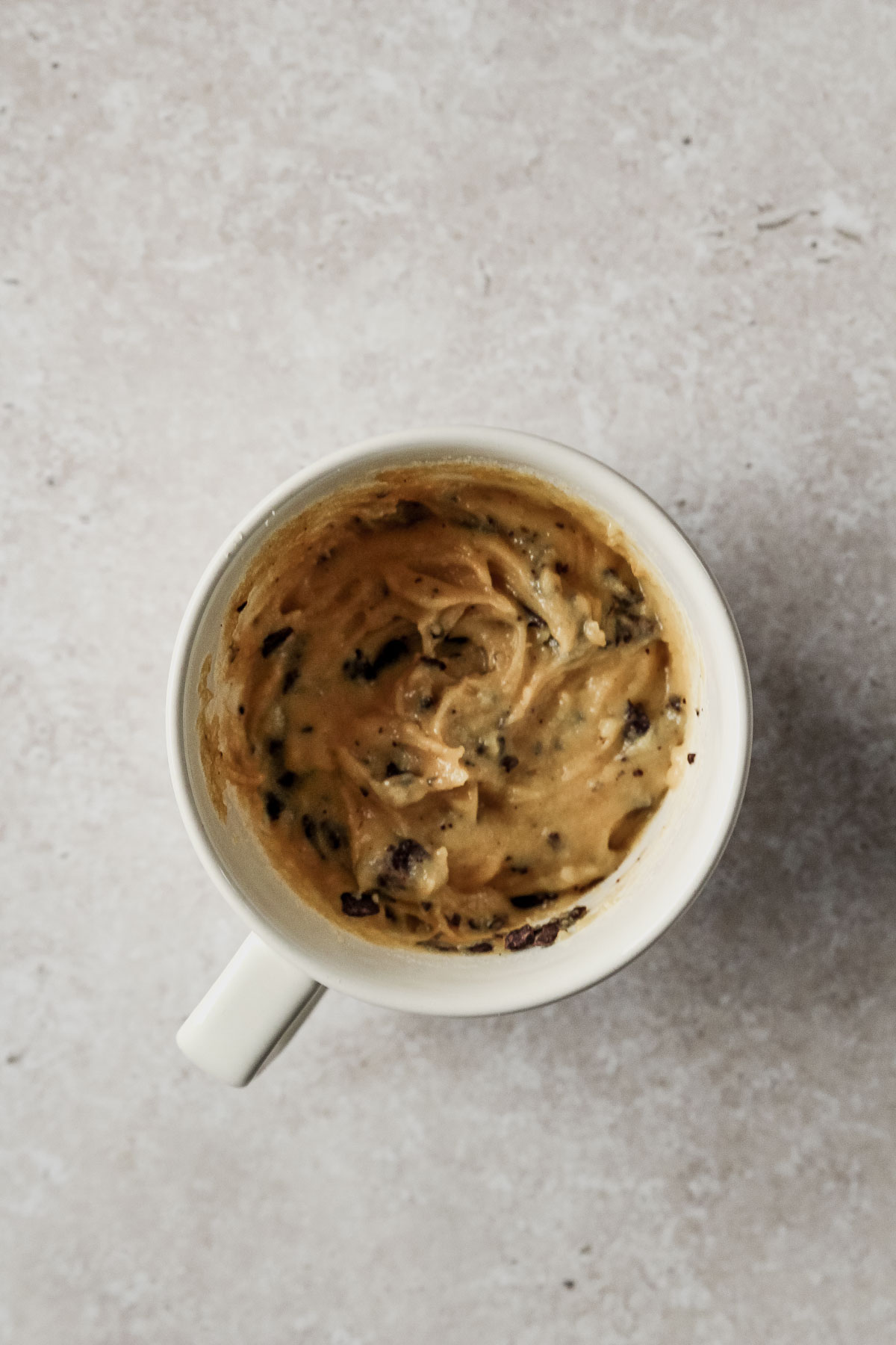 mixed dough for chocolate almond flour mug cake in off-white mug on beige marble background.