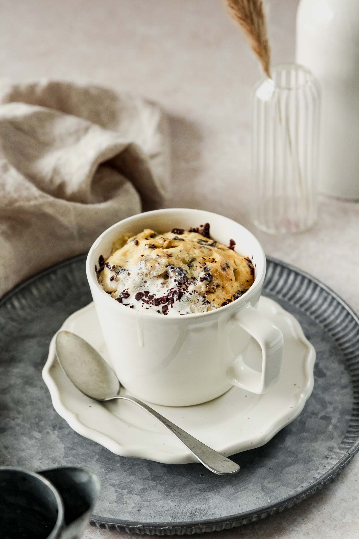 almond flour protein mug cake in off-white mug on vintage metal plate on beige marble background with props.