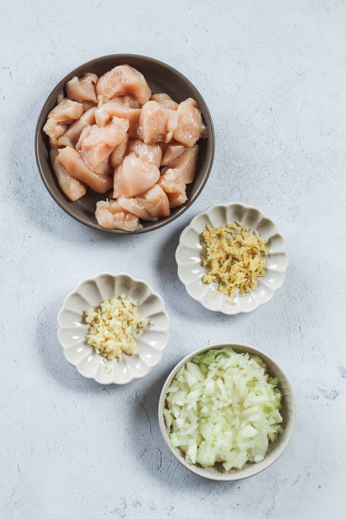 chopped chicken breast, onion, garlic and ginger in bowls.