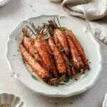 roasted carrots on a light beige serving platter with herbs and spices.