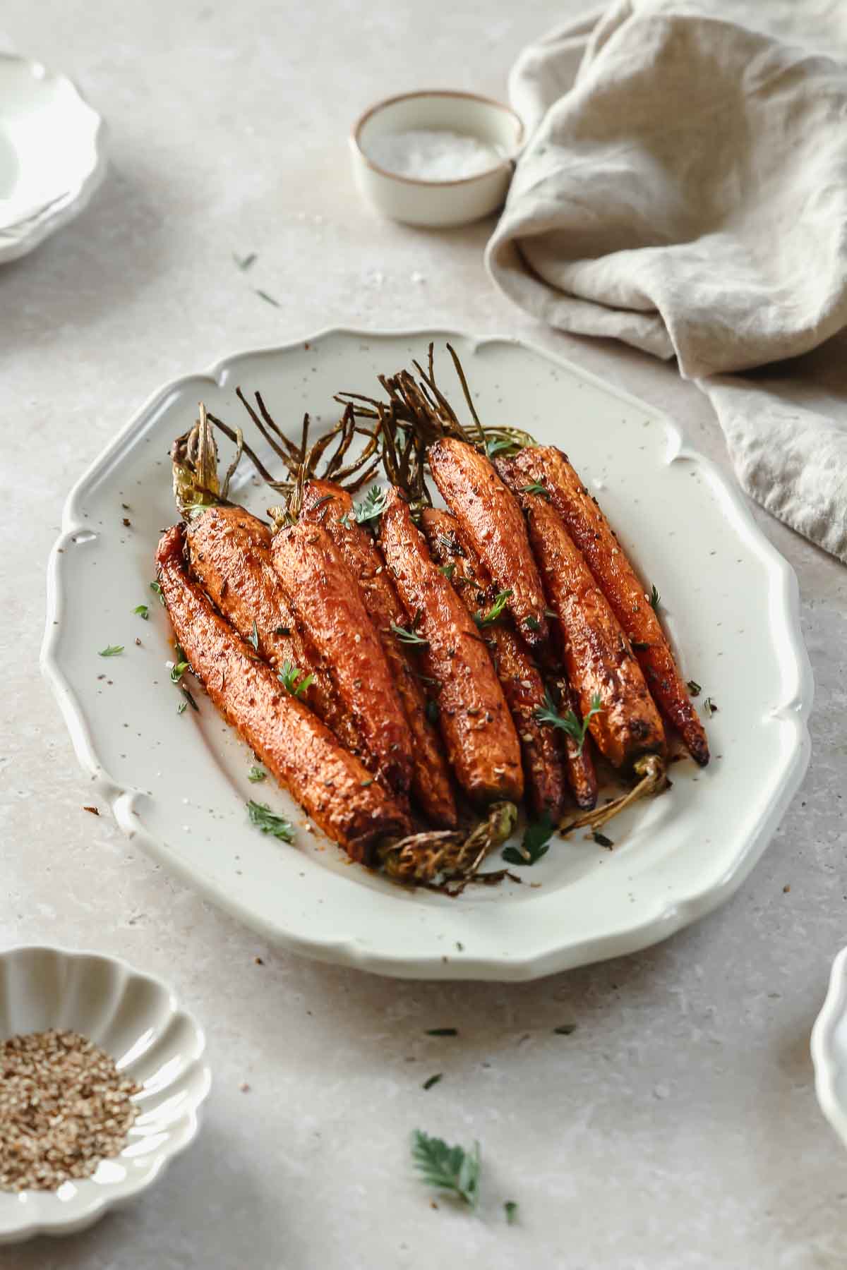 roasted carrots on a light beige serving platter with herbs and spices.