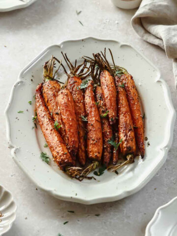 roasted carrots on a light beige serving platter with herbs and spices.