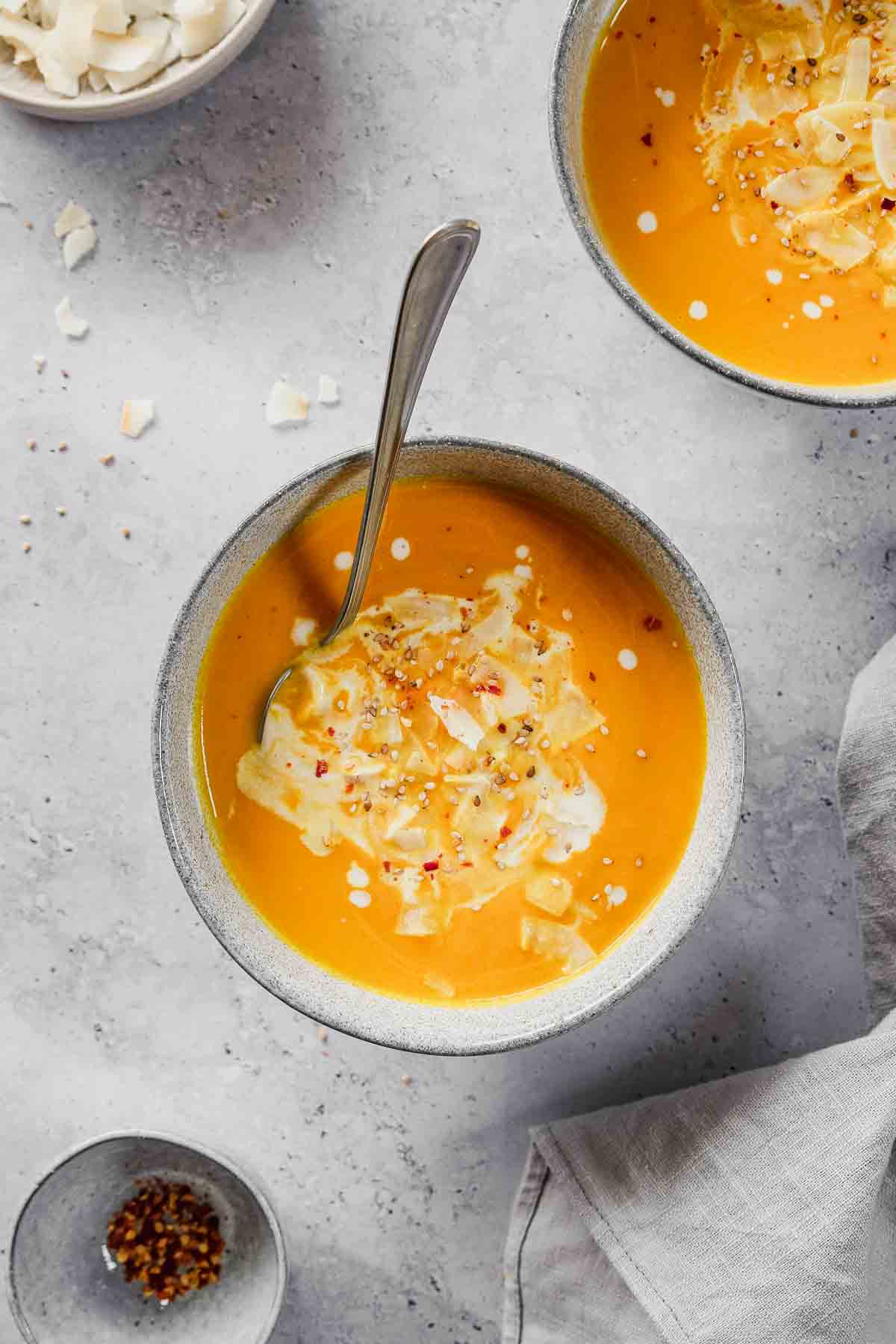 curried carrot ginger coconut soup in blue bowl with toppings and vintage spoon.