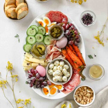 easy easter charcuterie board placed on grey background with props and spring flowers.