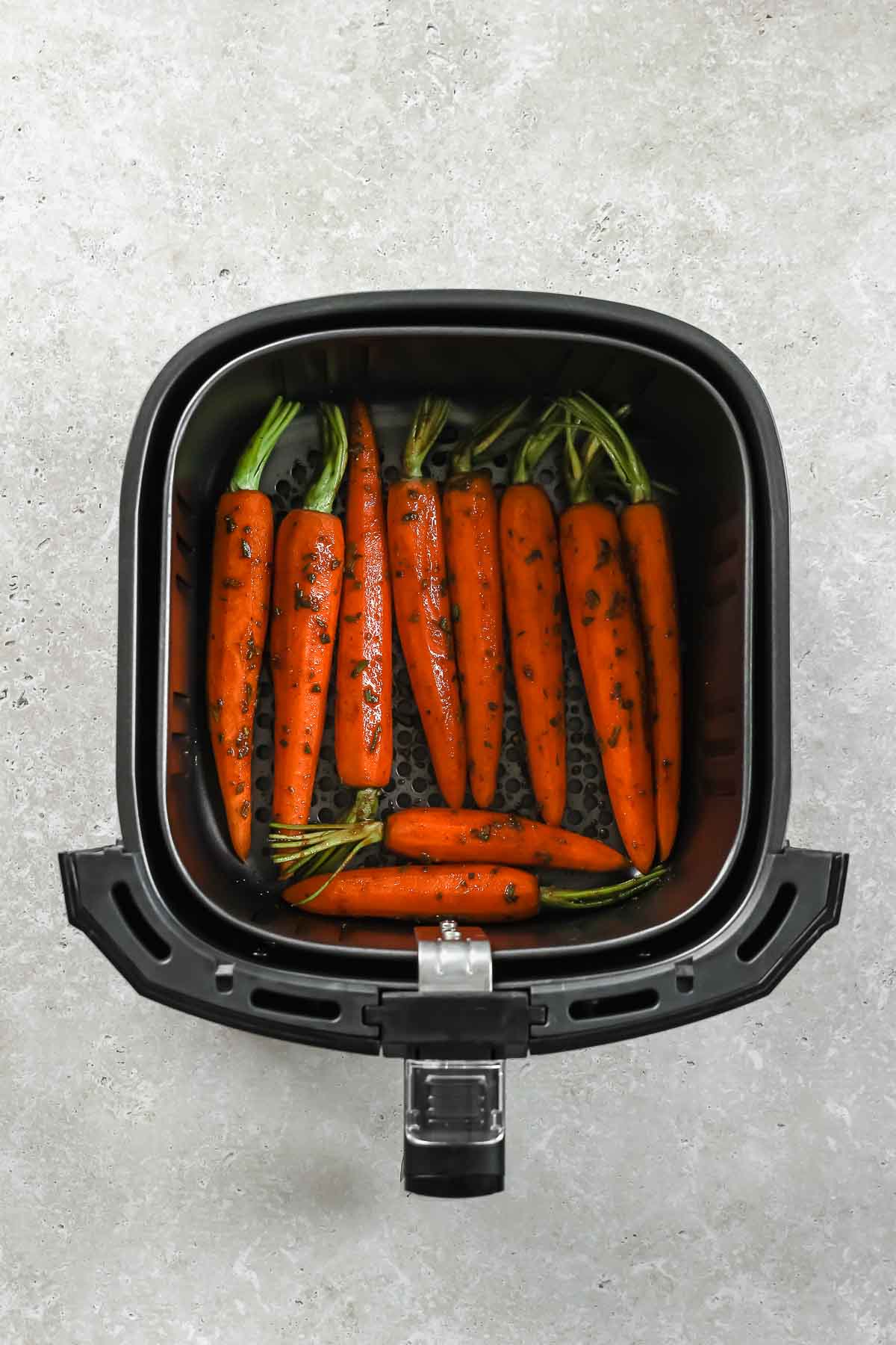 seasoned carrots arranged in an air fryer before baking.