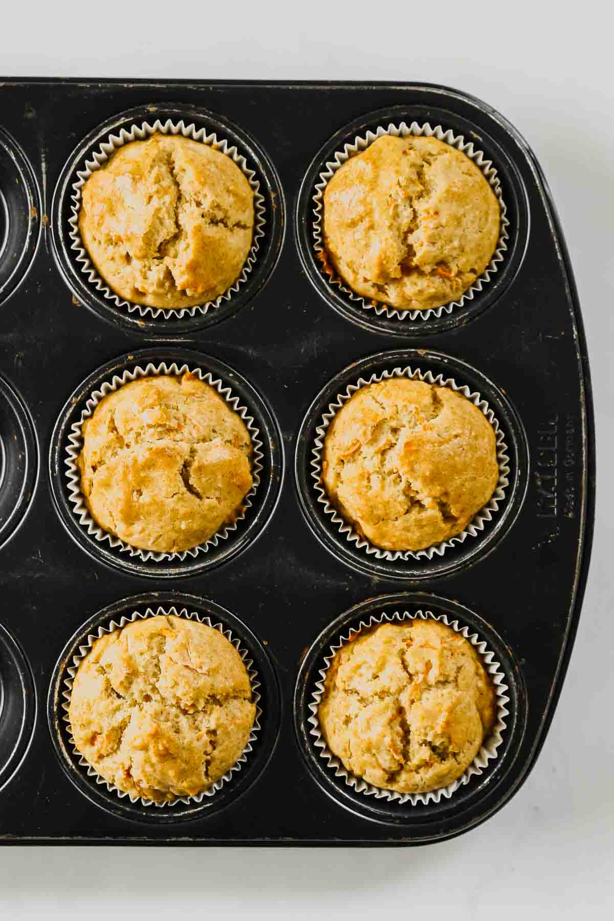 baked carrot cake muffins in black muffin tin.