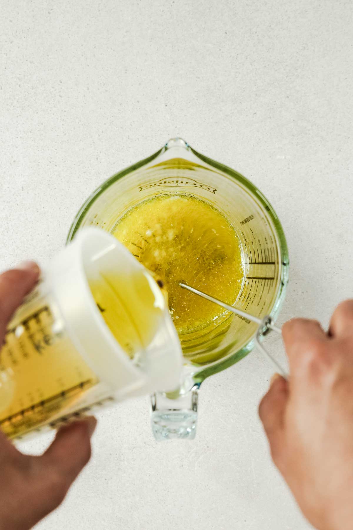 pouring olive oil into ingredients for vinaigrette while whisking.