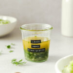 simple herb vinaigrette in weck jar with salads and props in background.