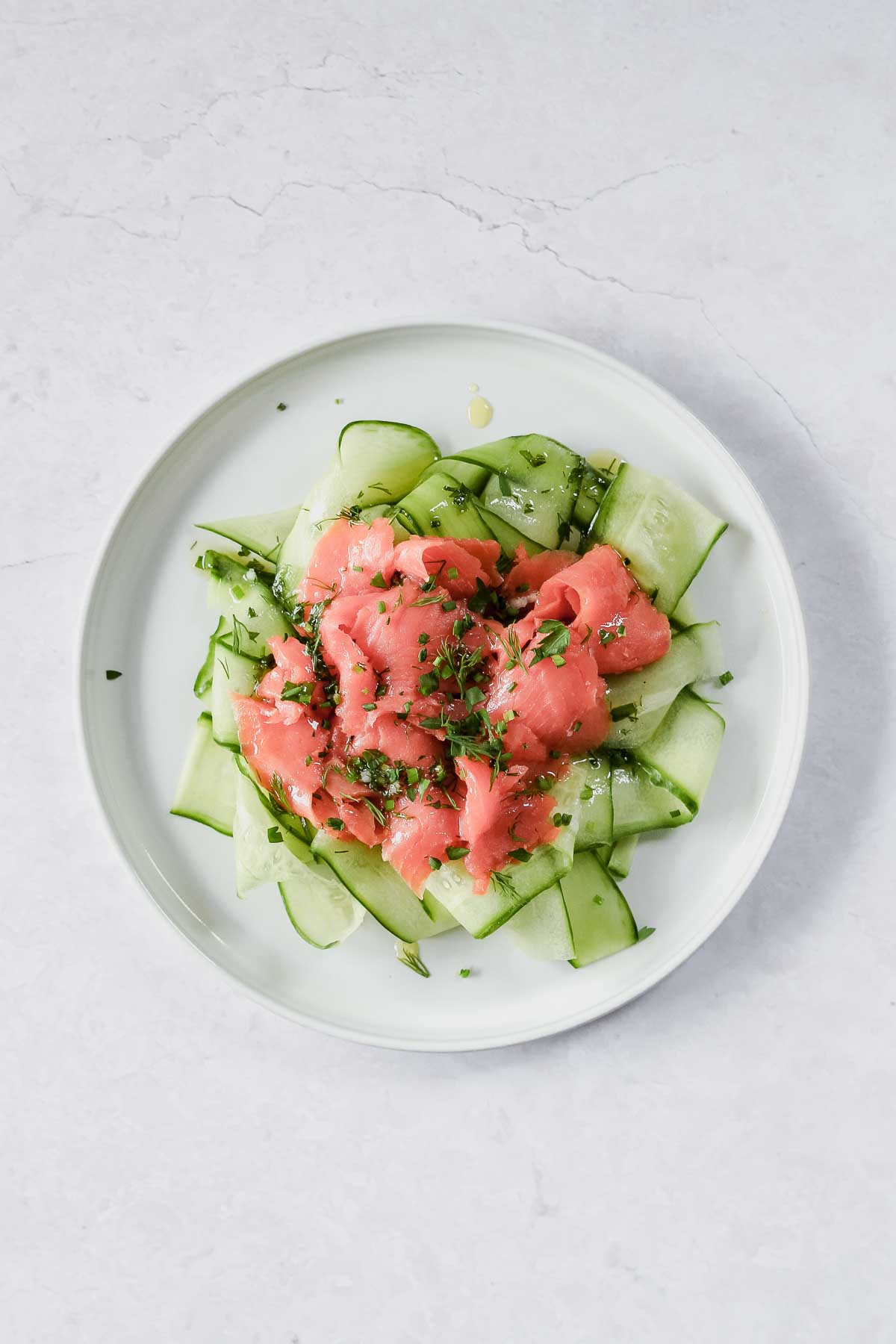 sliced cucumber, smoked salmon, and herb vinaigrette arranged on white plate.