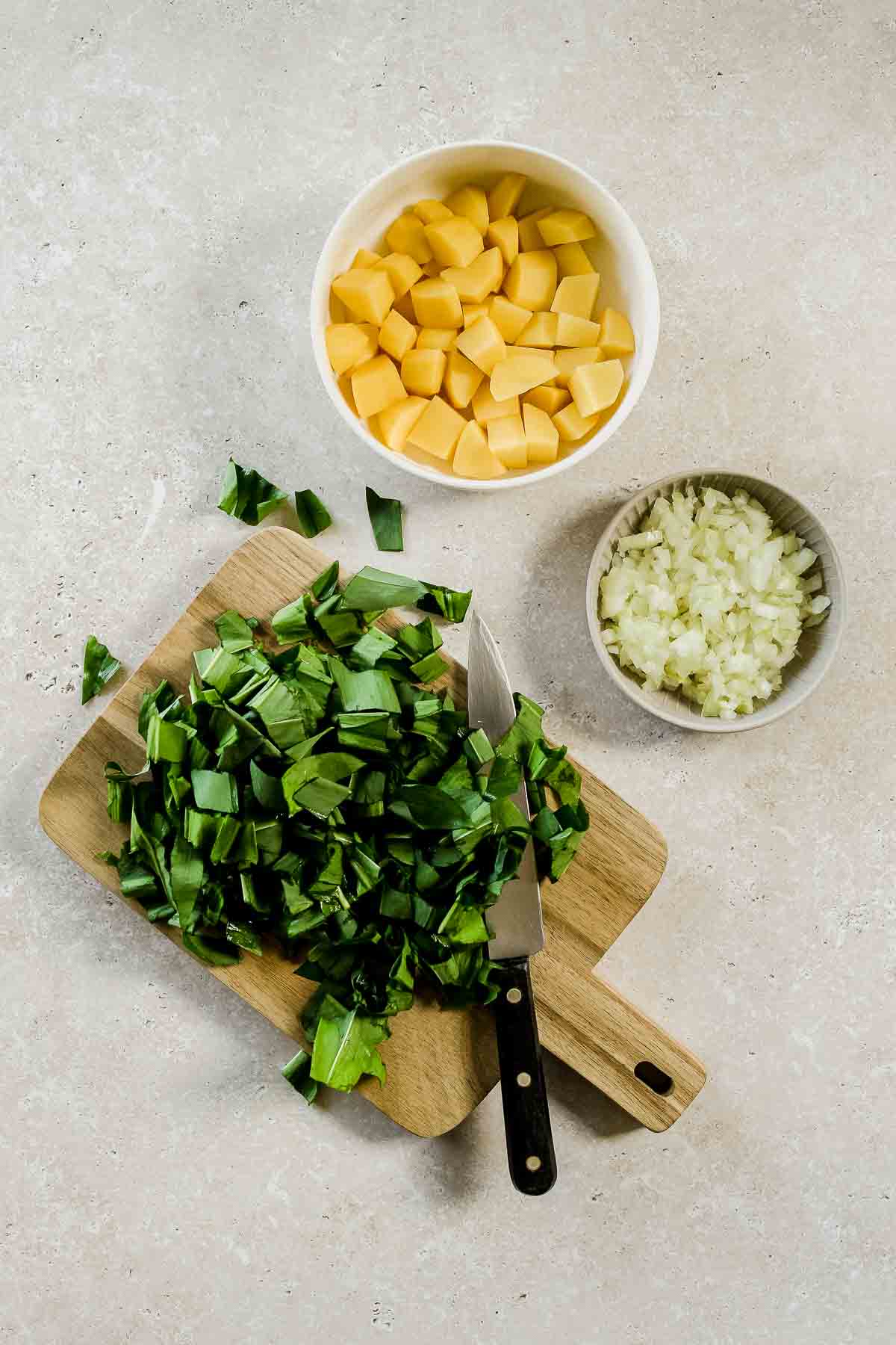 chopped wild garlic, potatoes, and onion on beige marble background.