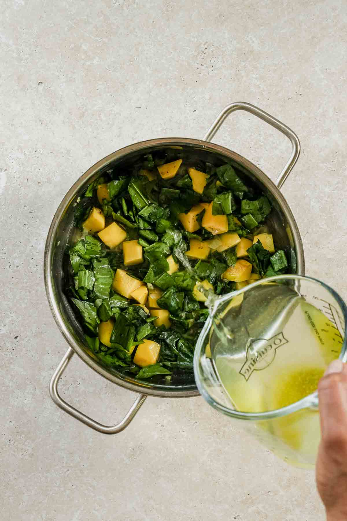 pouring vegetable stock into a pot with roasted wild garlic, potatoes, and onion.