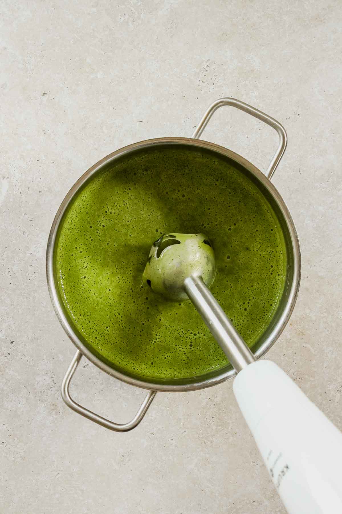 pureeing wild garlic and potato soup with a stick blender in the pot.