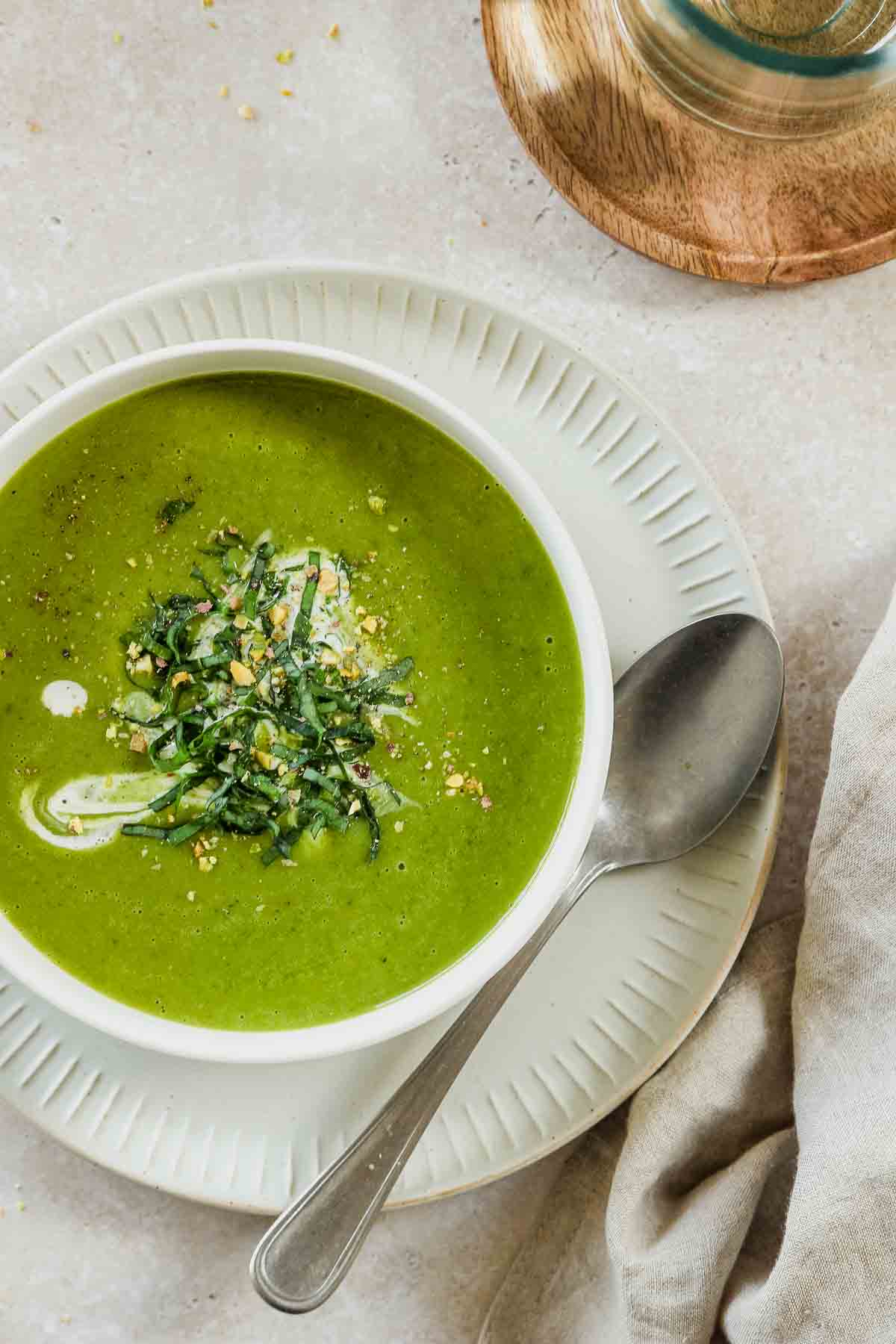 bright green wild garlic and potato soup in a white bowl with a vintage spoon on a plate with props.