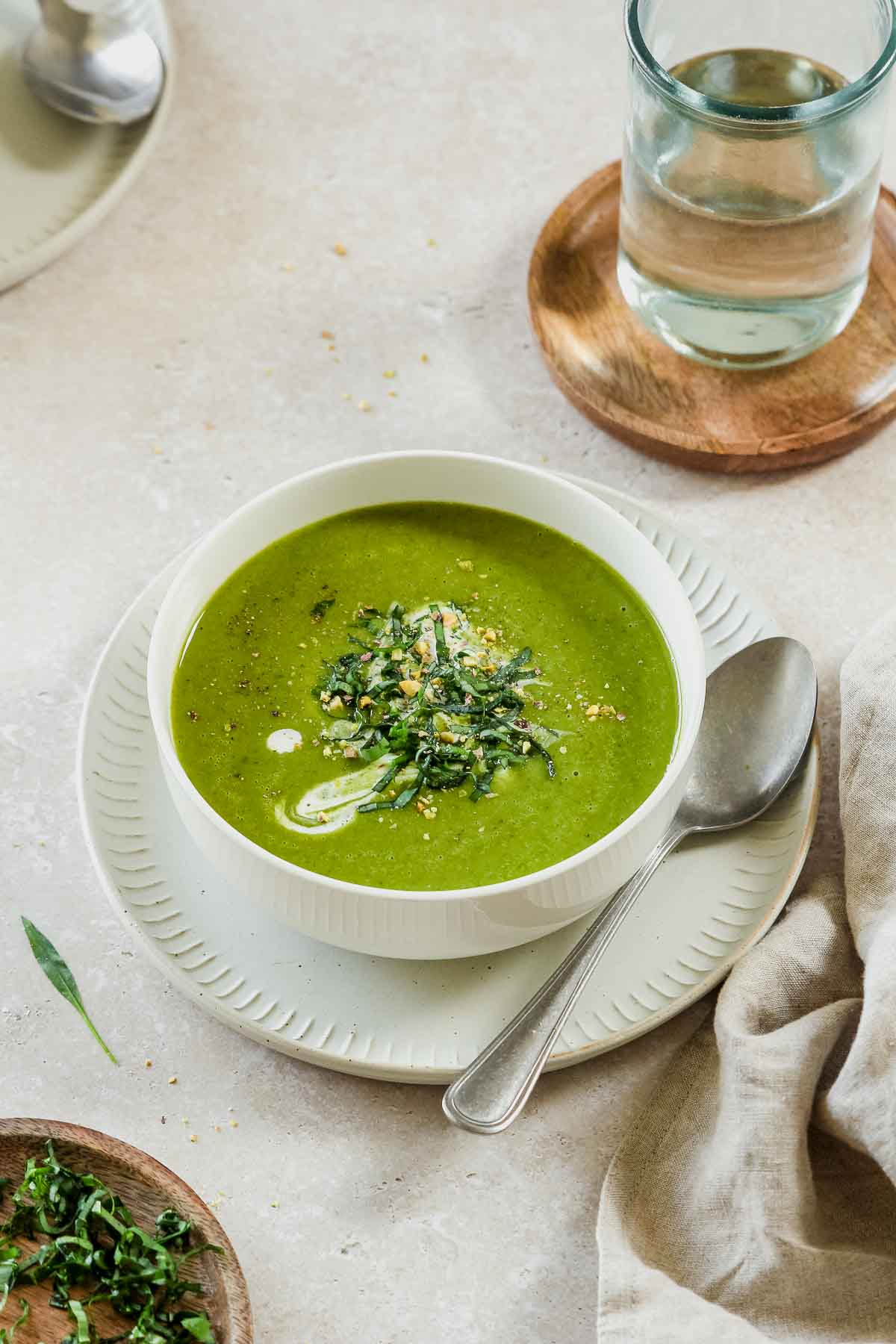 bright green wild garlic and potato soup in a white bowl with a vintage spoon on a plate with props.