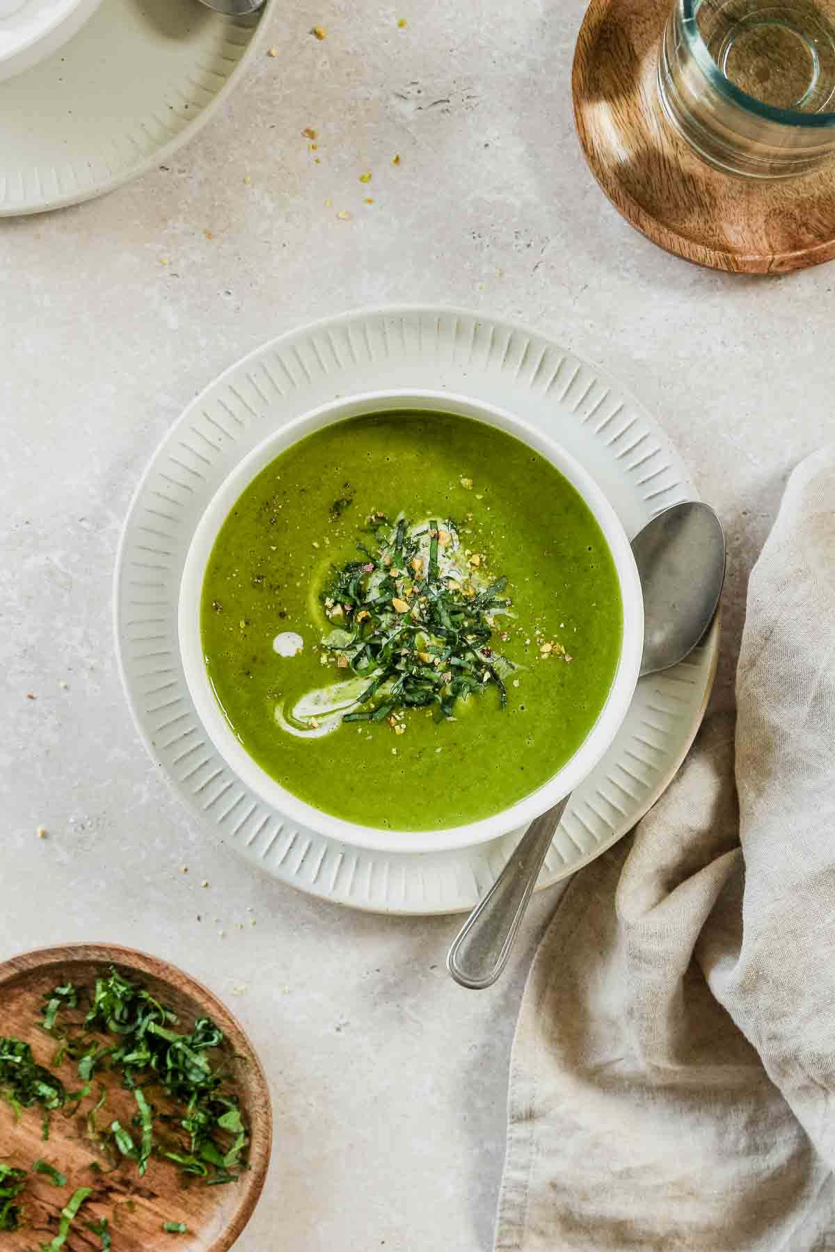 wild garlic soup in a white bowl on a beige background with props.