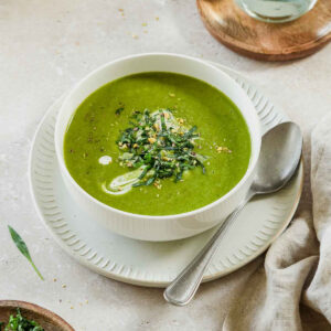 wild garlic soup in a white bowl on a beige background with props.