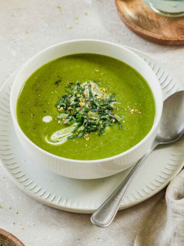 wild garlic soup in a white bowl on a beige background with props.