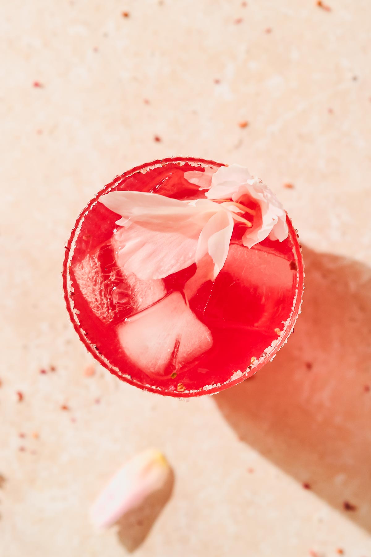 overhead shot of raspberry gin cocktail with peony leaves decoration on beige background.