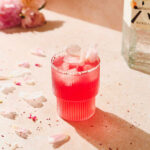 raspberry gin cocktail with peony leaves decoration on beige background.