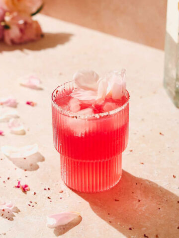 raspberry gin cocktail with peony leaves decoration on beige background.