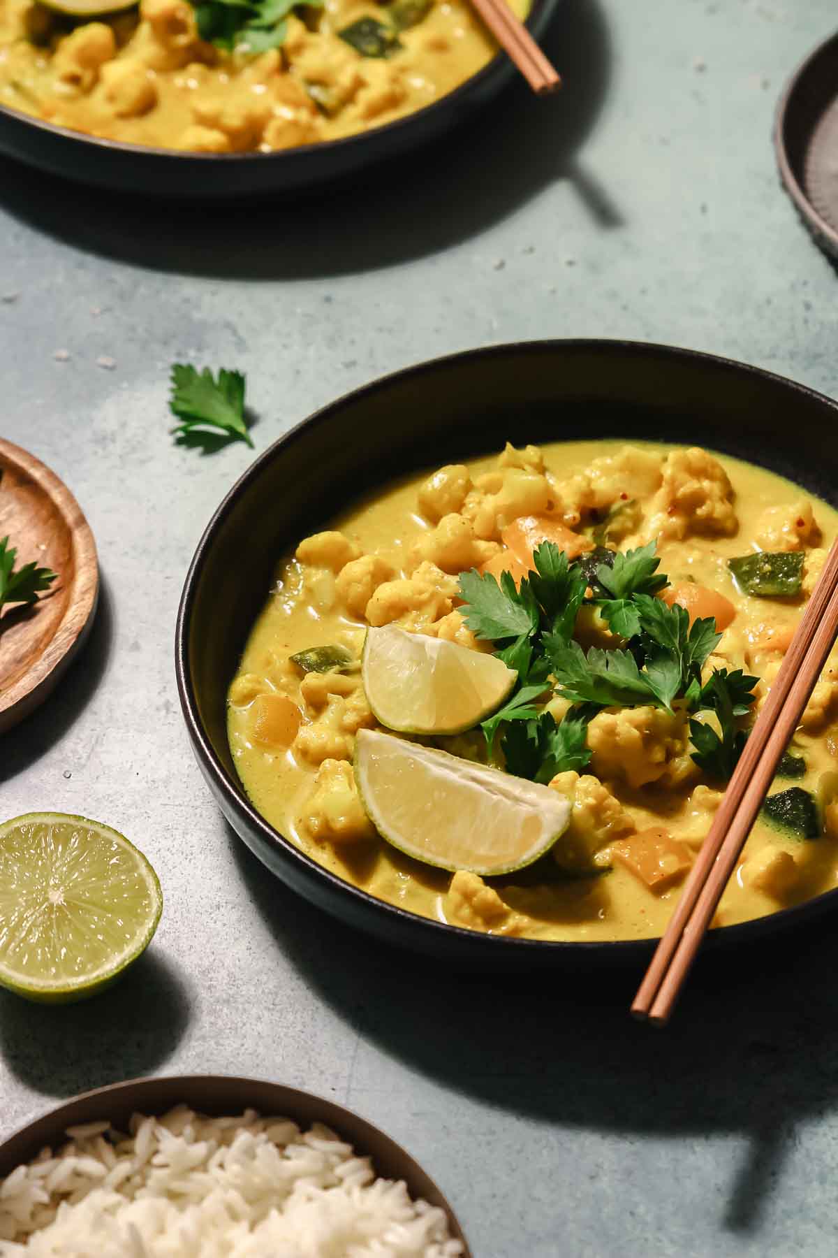 vegan yellow curry in black bowl with chopsticks on turquoise background.