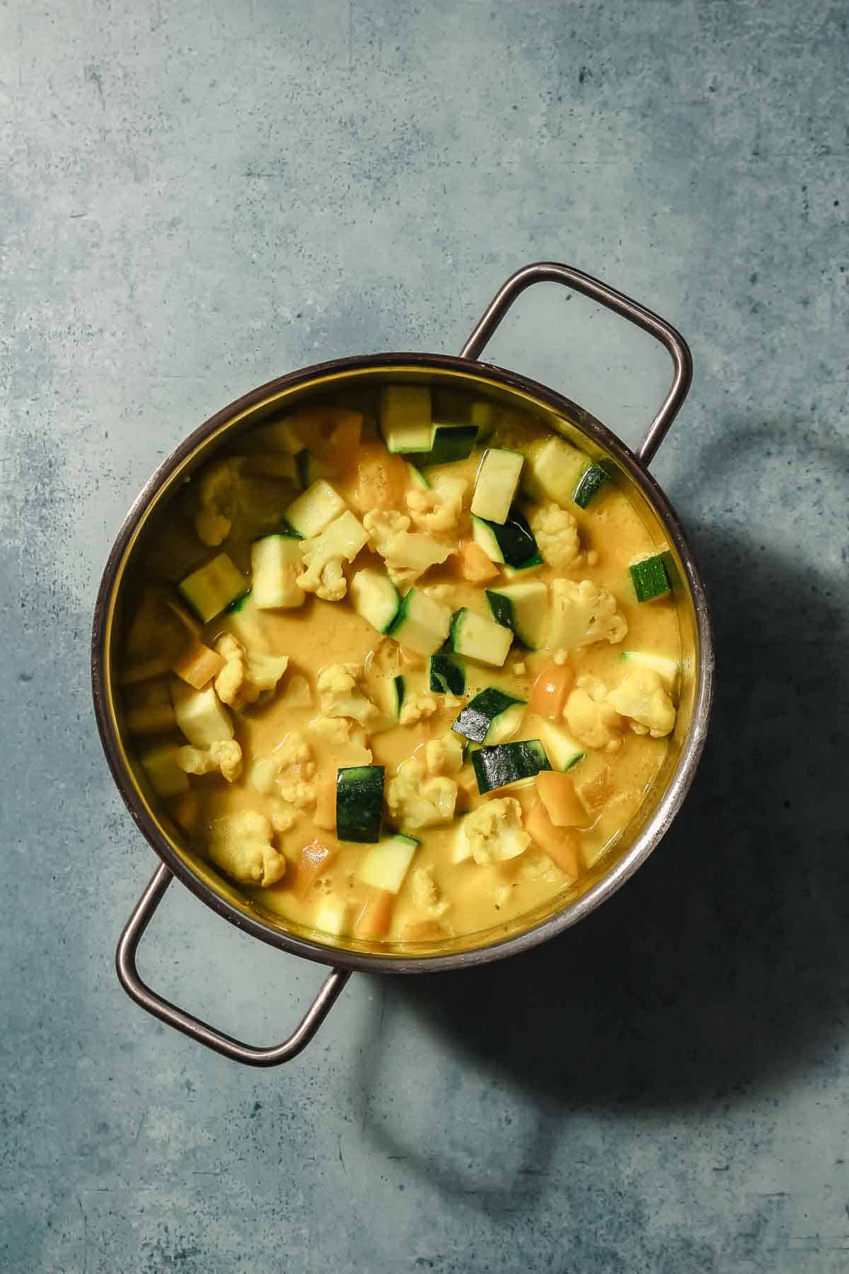 zucchini, bell pepper and cauliflower cooking in pot with Thai curry spices and coconut milk.