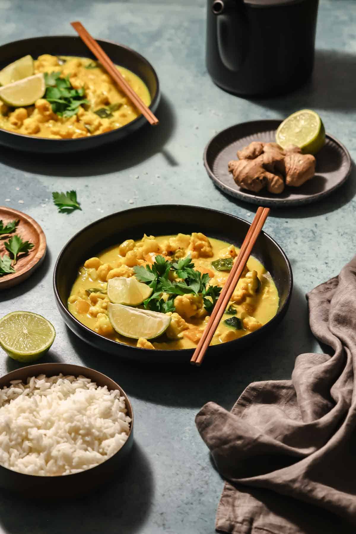 vegan Thai yellow vegetable curry in black bowls with chopsticks on turquoise background.