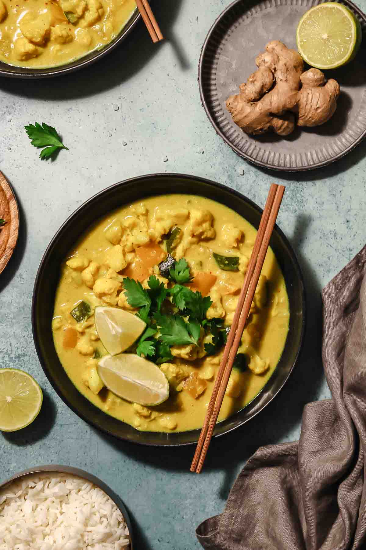 vegan Thai yellow vegetable curry in black bowls with chopsticks on turquoise background.