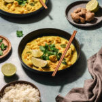 healthy vegetable curry on black bowl with chopsticks on turquoise background.