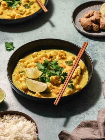 healthy vegetable curry on black bowl with chopsticks on turquoise background.