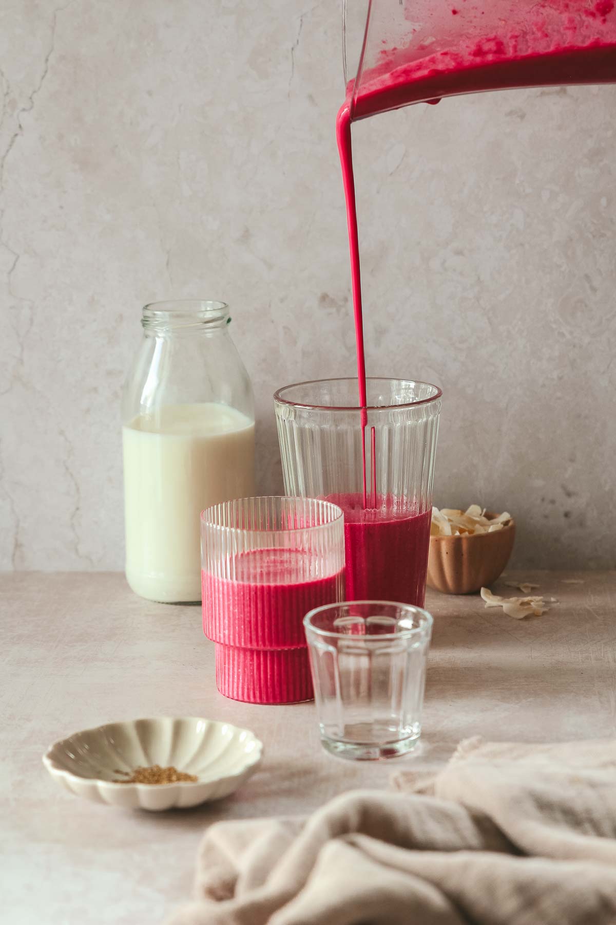 pink breakfast smoothie poured into glassed on beige-pink backdrop with props.